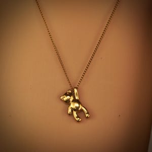 May include: A gold-coloured teddy bear pendant necklace. The bear hangs from a delicate chain. The necklace is a simple, elegant piece of jewellery.