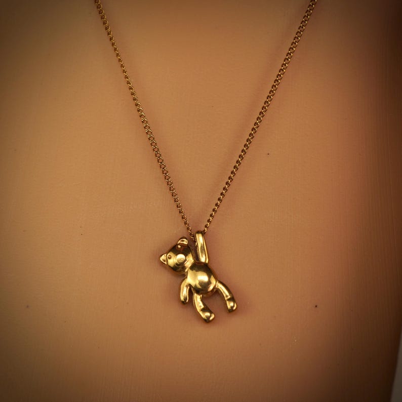 May include: A gold-coloured teddy bear pendant necklace. The bear hangs from a delicate chain. The necklace is a simple, elegant piece of jewellery.