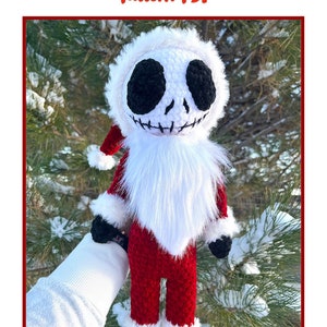 Op de afbeelding: Haakpatroon voor een kerstman Jack Skellington pop. De pop is gekleed in een rood pak met witte bontkraag en een zwarte hoed. De pop heeft een wit gezicht met zwarte ogen en een gestikte glimlach.