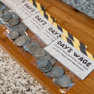 May include: A plastic bag filled with silver coins with a printed tag that reads "Day's Wage" with the text "Thanks for being part of our 'crew.' Hope you had a 'diggin' good time at work!"