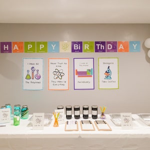 May include: A science-themed birthday party decoration with a banner that reads "HAPPY Bi Ra Th D A Y" using the periodic table elements. There are five posters with science puns and illustrations. The table is decorated with jars of blue and green liquid, jars of black liquid, and signs with the periodic table symbol for science.