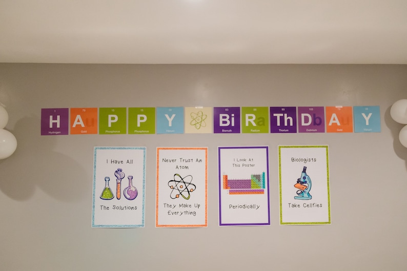 May include: A wall decorated with colorful science-themed birthday decorations. The decorations feature the periodic table of elements and science puns. The text on the wall reads "HAPPY BIRTHDAY".