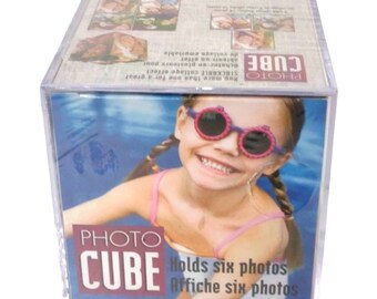 May include: Clear Photo Cube with the words "Photo Cube" in red and white. The cube holds six photos and features a smiling girl wearing pink sunglasses. The cube is designed to display multiple photos.