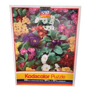 May include: A 550-piece jigsaw puzzle featuring a close-up of a variety of colorful primrose flowers. The puzzle is called "Kodacolor Puzzle" and is 18 15/16 inches by 20 1/8 inches when assembled.