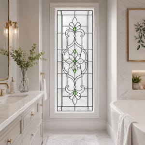Puede incluir: Una ventana rectangular con un inserto de vidriera decorativa con un patrón simétrico floral y de volutas en vidrio texturizado transparente, acentuado por cuatro pequeñas joyas de vidrio verde vibrante en un marco de metal negro.