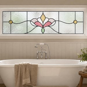 Könnte beinhalten: Ein rechteckiges Buntglas-Fensterpaneel mit einem zentralen Blumenmotiv in sanften Rosa-, Gelb- und Grüntönen. Das Design ist von klaren, strukturierten Glasscheiben umrahmt und mit zwei runden, goldfarbenen Glasjuwelen an den Seiten akzentuiert.