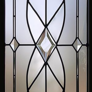 Może przedstawiać: Dekoracyjny panel szklany o geometrycznym wzorze. Panel posiada przezroczyste szklane sekcje obrysowane czarnymi liniami, tworząc kształty romb&oacute;w, owali i tr&oacute;jkąt&oacute;w. Projekt jest symetryczny i nowoczesny.