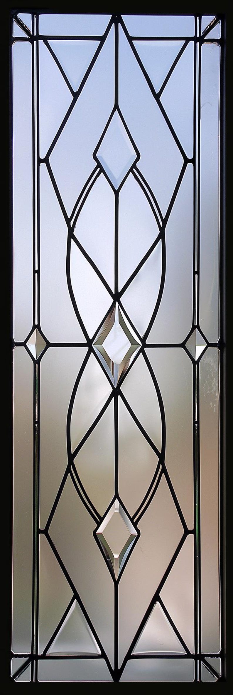 Może przedstawiać: Dekoracyjny panel szklany o geometrycznym wzorze. Panel posiada przezroczyste szklane sekcje obrysowane czarnymi liniami, tworząc kształty romb&oacute;w, owali i tr&oacute;jkąt&oacute;w. Projekt jest symetryczny i nowoczesny.