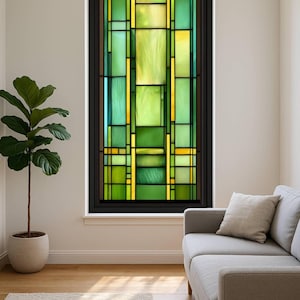 May include: A stained glass window with a black frame, featuring a geometric design in shades of green and yellow. The window is installed in a room with a neutral colour palette, a sofa, and a potted plant.