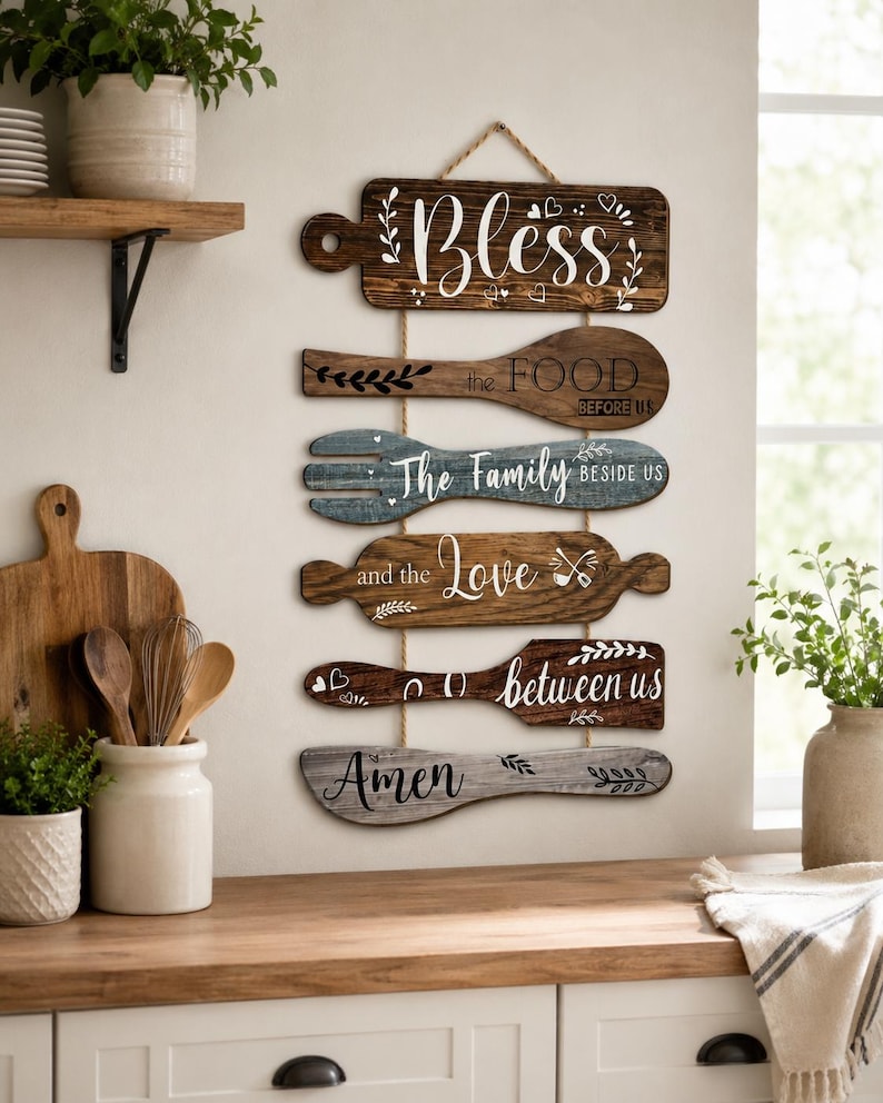 Peut inclure: Une d&eacute;coration murale verticale compos&eacute;e de six plaques en bois en forme d'ustensiles de cuisine reli&eacute;es par une corde. Les plaques portent les inscriptions : Bless, the FOOD BEFORE US, The Family BESIDE US, and the Love, between us, et Amen.