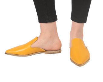 May include: A pair of yellow leather pointed-toe mules with a low heel. The mules are made of a soft, supple leather and have a comfortable fit.