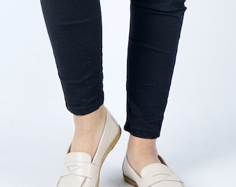 May include: A pair of light beige leather loafers with a simple design. The loafers have a rounded toe and a low heel.
