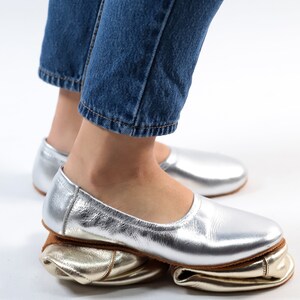 Puede incluir: Un par de bailarinas de cuero plateado con forro de cuero dorado. Las bailarinas est&aacute;n dobladas hacia abajo para crear un look &uacute;nico.