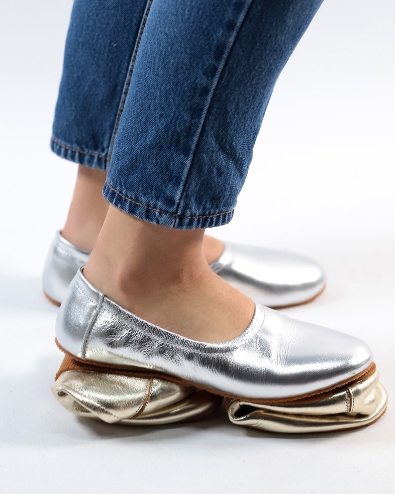 Puede incluir: Un par de bailarinas de cuero plateado con forro de cuero dorado. Las bailarinas est&aacute;n dobladas hacia abajo para crear un look &uacute;nico.