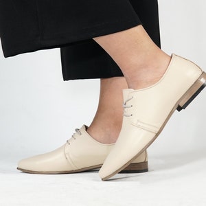 May include: A pair of cream-colored leather lace-up shoes with a slightly pointed toe and a low heel.