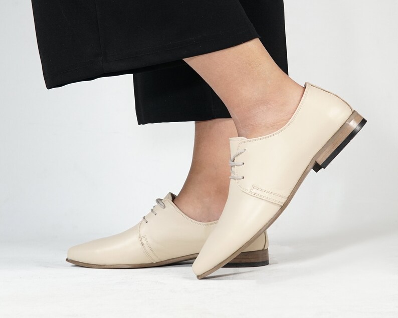 May include: A pair of cream-colored leather lace-up shoes with a slightly pointed toe and a low heel.