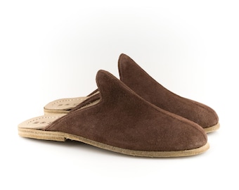 May include: A pair of brown suede slippers with a leather sole. The slippers are closed-toe and have a simple design.