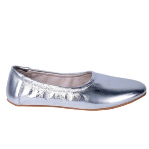 Puede incluir: Un par de bailarinas plateadas de punta redonda y suela plana.