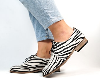 May include: Black and white zebra print lace-up shoes with a brown leather sole.