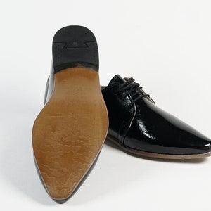 May include: A pair of black patent leather dress shoes with lace-up closures. The shoes have a pointed toe and a low heel.