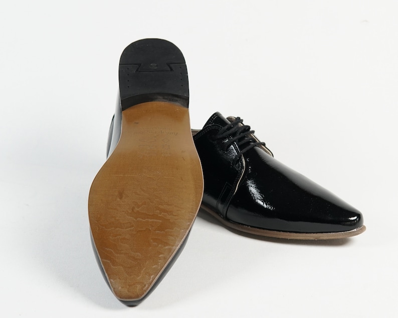 May include: A pair of black patent leather dress shoes with lace-up closures. The shoes have a pointed toe and a low heel.