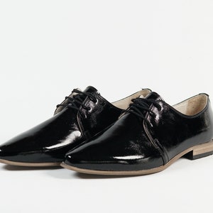 May include: Pair of black patent leather lace-up shoes with a pointed toe and a low heel.