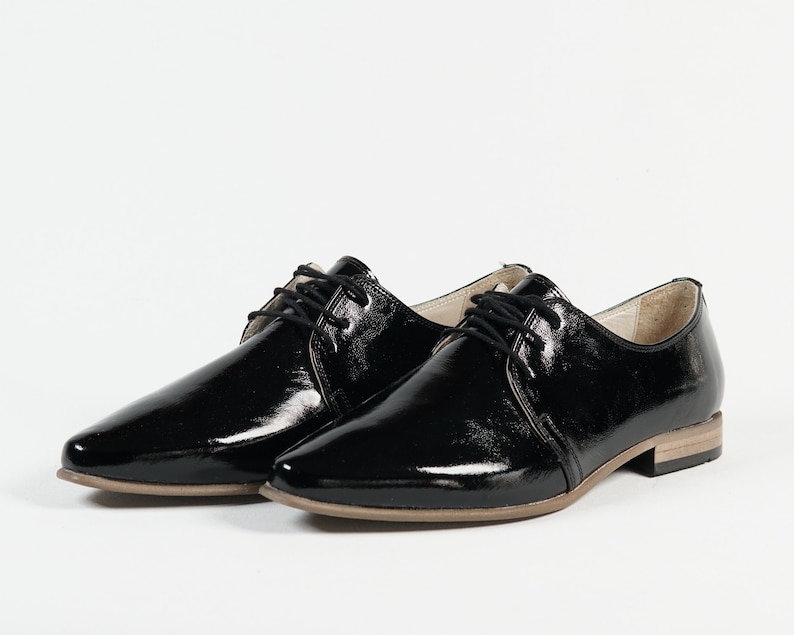 May include: Pair of black patent leather lace-up shoes with a pointed toe and a low heel.