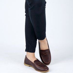 May include: A pair of brown leather loafers with a tassel detail. The loafers are worn with black pants.