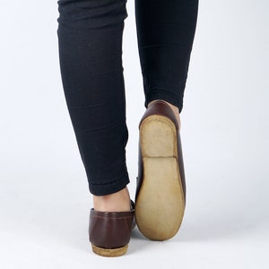 May include: A pair of brown leather loafers with a light brown sole. The loafers are worn by a person wearing black pants.