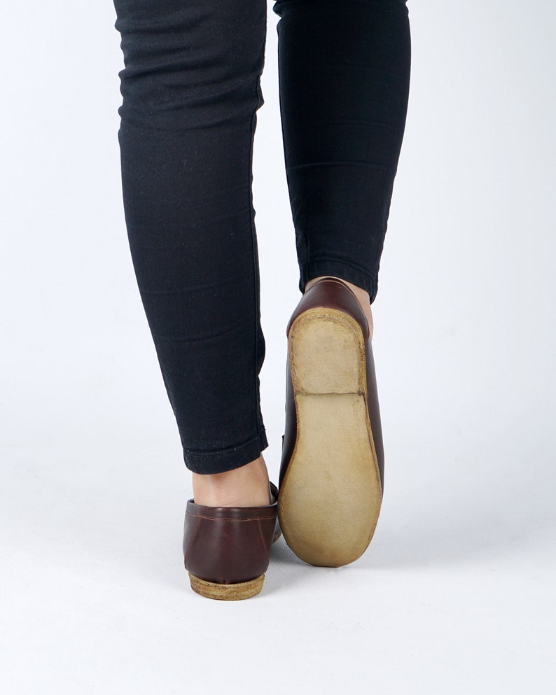 May include: A pair of brown leather loafers with a light brown sole. The loafers are worn by a person wearing black pants.