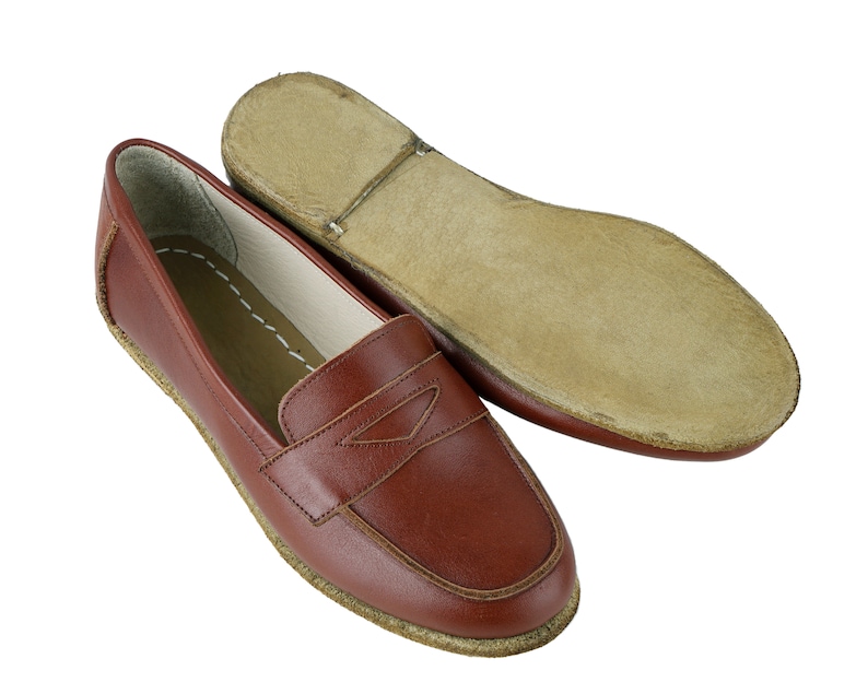 May include: A pair of brown leather loafers with a stitched detail on the front. The loafers have a leather sole and a slightly rounded toe.