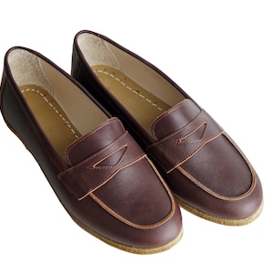 May include: A pair of brown leather loafers with a subtle stitch detail on the vamp. The loafers have a rounded toe and a low heel.