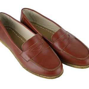 May include: A pair of brown leather loafers with a simple design. The loafers have a stitched seam around the edge of the shoe and a small decorative detail on the top.