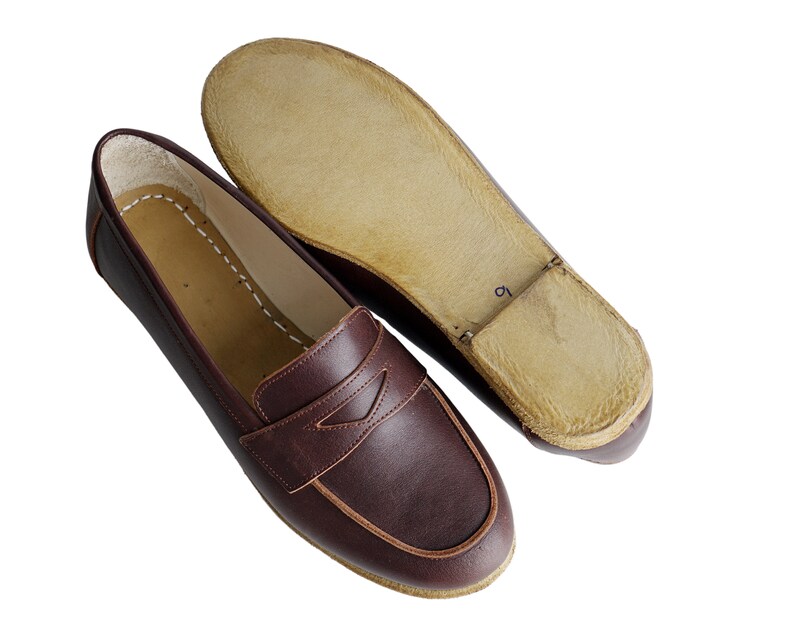 May include: A pair of brown leather loafers with a brown leather sole. The loafers have a simple design with a single strap across the top.
