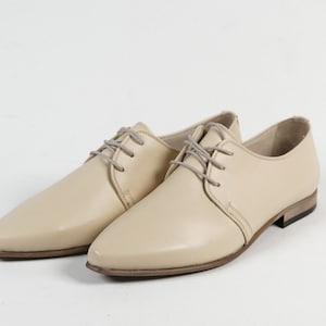 May include: A pair of beige leather lace-up shoes with a pointed toe and a low heel.