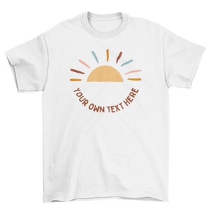 May include: White t-shirt featuring a sun design with a half-circle and colorful rays. The sun is a light orange color, and the rays are in shades of pink, blue, and brown. The text "YOUR OWN TEXT HERE" is in a brown font.