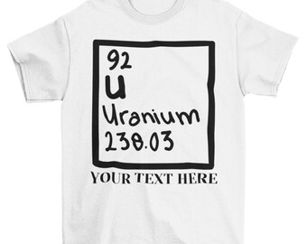 May include: White t-shirt with a black and white graphic of a periodic table element. The element is Uranium (U) with the atomic number 92 and atomic weight 238.03. The text "YOUR TEXT HERE" is printed below the graphic.
