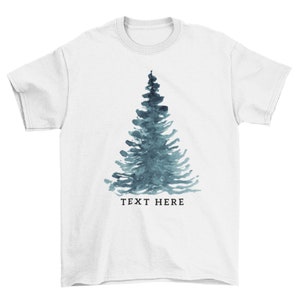 May include: White t-shirt with a blue watercolor pine tree design and the text "TEXT HERE" below the tree.