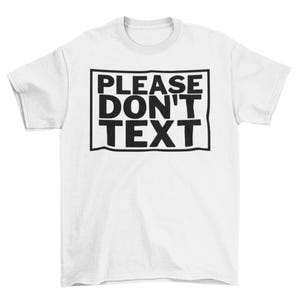 May include: White t-shirt with the text "PLEASE DON'T TEXT" in a black, bold font inside a black rectangular border. The shirt has short sleeves and a crew neck.