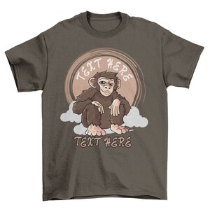 May include: A brown t-shirt with a cartoon image of a monkey sitting on a cloud. The text "TEXT HERE" appears above and below the monkey.