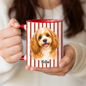 May include: A red and white striped mug featuring a Cavalier King Charles Spaniel illustration with the name "Bella" below. The mug has a red interior and handle, perfect for coffee or tea.