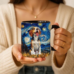 May include: A black-handled coffee mug featuring a beagle dog portrait in the style of Van Gogh's "Starry Night." The dog has brown and white fur, with its tongue out. The name "Bella" is written on the mug.