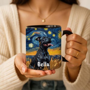 以下が含まれることがあります： 星空を背景に黒い犬のイラストが描かれた黒いセラミックマグカップ。マグカップには黒いハンドルと「Bella」という名前が白で書かれています。有名な絵画を彷彿とさせるデザインです。