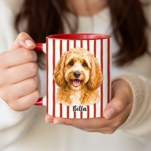 Puede incluir: Una taza de cerámica con un patrón de rayas verticales rojas y blancas que presenta una ilustración detallada de un perro de pelaje rizado color marrón dorado. Debajo del perro, el nombre Bella está impreso en cursiva negra. Asa roja.