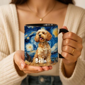 May include: A black-handled coffee mug featuring a dog portrait in the style of Van Gogh's "Starry Night." The mug has a blue background with swirling yellow stars and a happy dog with the name "Bella" on it.