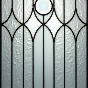 May include: Close-up of a decorative glass panel with a textured, frosted appearance. The design features black lines outlining geometric shapes, including diamonds and vertical bars, with a central teardrop-shaped element.