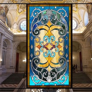 以下が含まれることがあります： 青、緑、黄色、茶色の幾何学模様のステンドグラスの窓。窓は金色の枠で囲まれ、白い背景に設置されています。