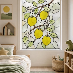 Op de afbeelding: Een raamfolie met een glas-in-loodontwerp van heldergele citroenen, groene bladeren en kleine witte bloemen. Het patroon bestaat uit donkere lijnen die doorschijnende secties scheiden, wat zorgt voor een botanisch motief op het raam.