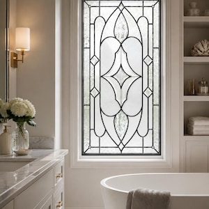 May include: A rectangular window featuring decorative leaded glass with a symmetrical, geometric pattern of clear and textured panes. The design consists of curved lines and diamond shapes framed by a dark metal border, set within a white wall.