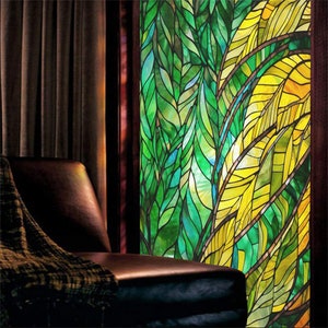 May include: A stained glass window with a design of green and yellow leaves. The window is in a room with a brown leather chair and a brown blanket.